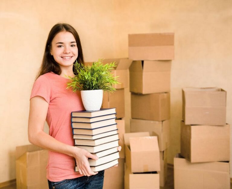 Girl holding stack of books with boxes behind her
