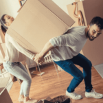 Two people cooperatively lifting a moving box from their living room