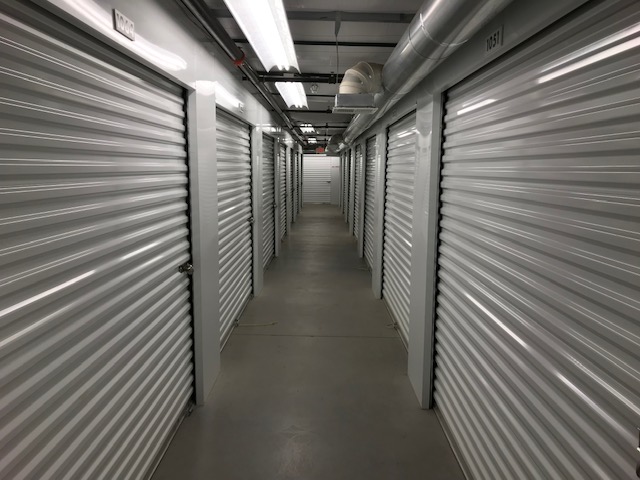 A well-lit and clean hallway of indoor storage units with white doors