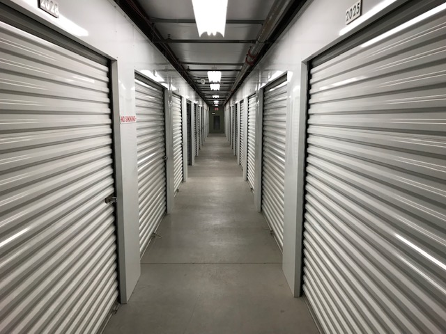 A well-lit hallway of large indoor storage units with white doors