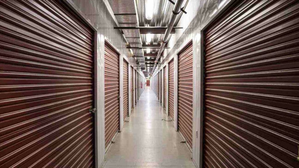 A very long, well lit hallway of large indoor storage units with red doors