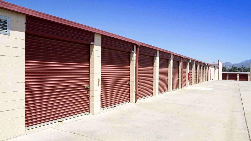 Row of outdoor storage units with large, red doors in a secure area