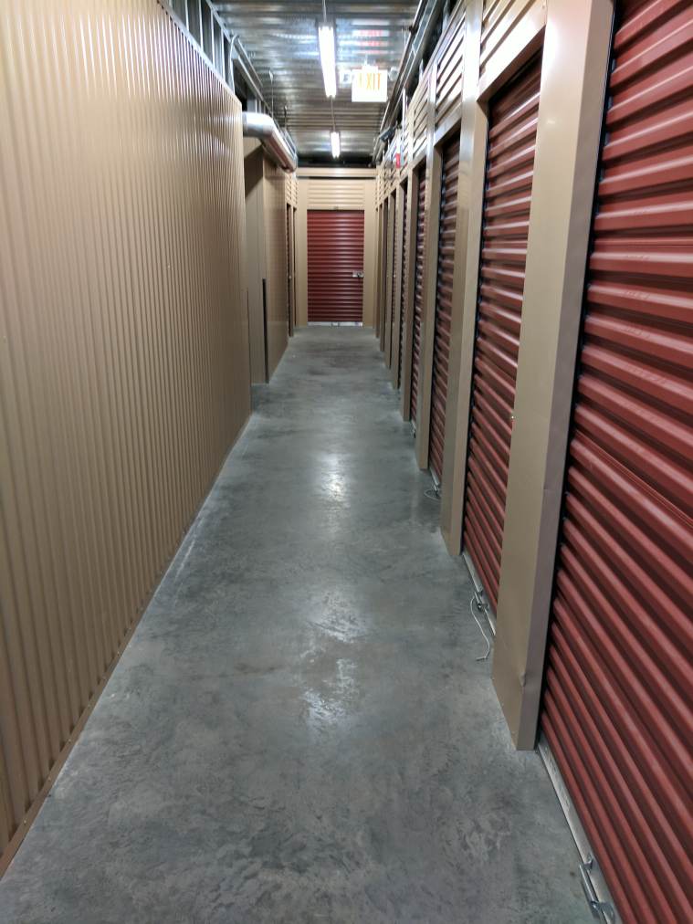 A well-lit hallway of small indoor storage units with red doors