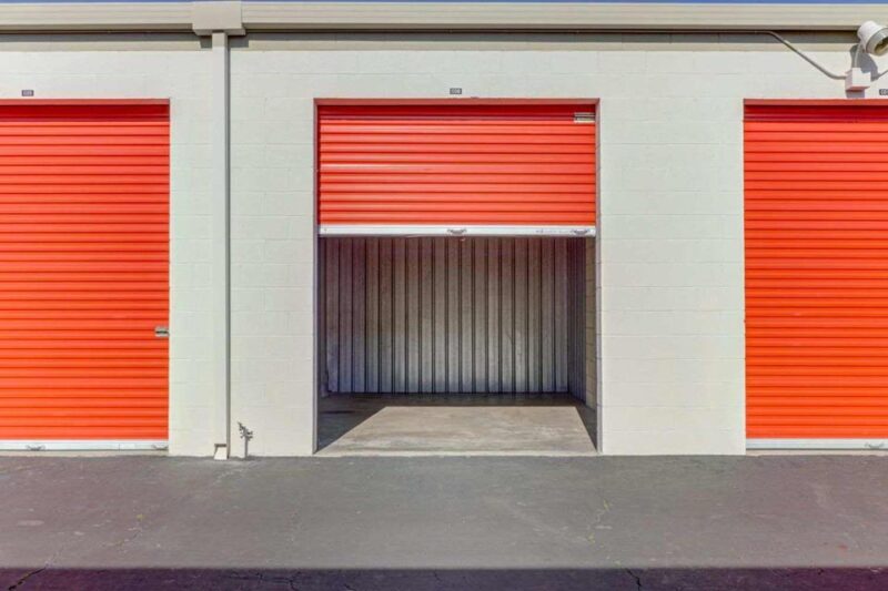 Outdoor storage units with large orange doors with one door open to a clean, empty unit