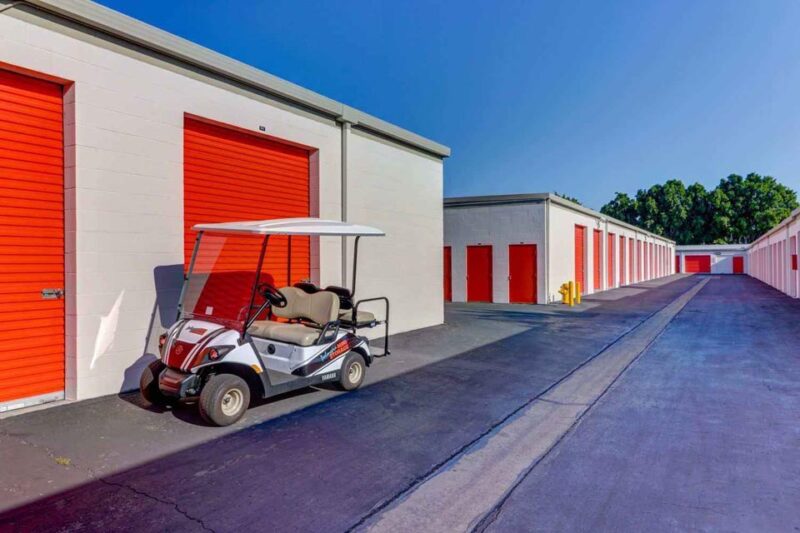A long row of large outdoor storage units with orange doors in a clean area