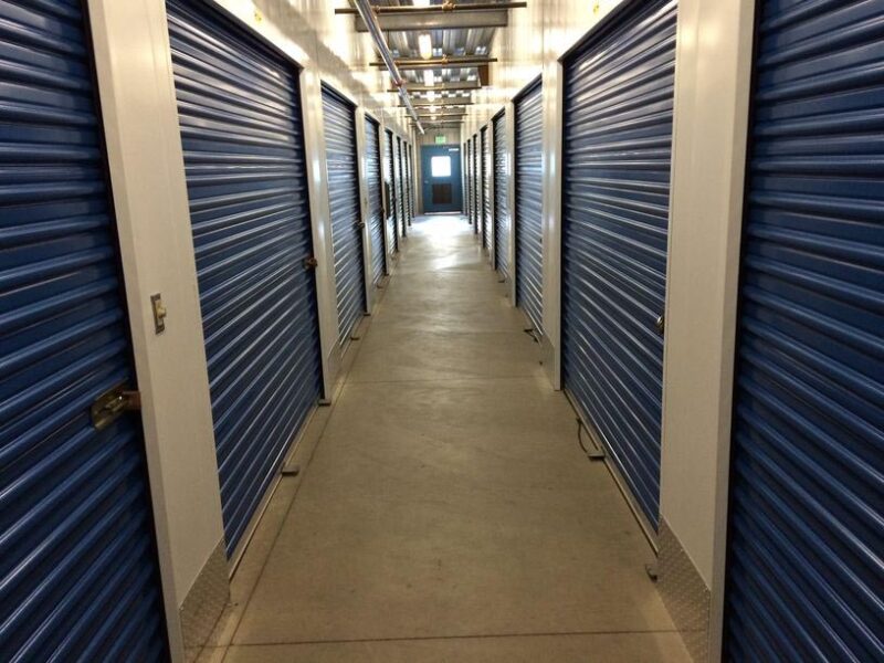 A well-lit hallway of large indoor storage units with blue doors