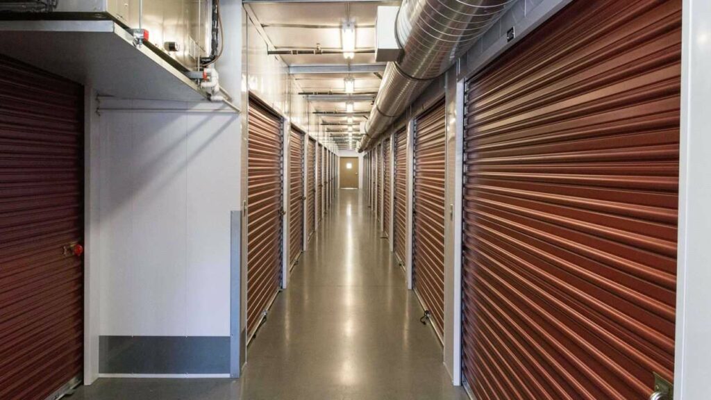A long row of large indoor storage units with red doors in a well-lit and clean hallway