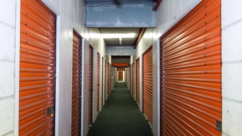 A long row of indoor storage units with orange doors in a well lit hallway