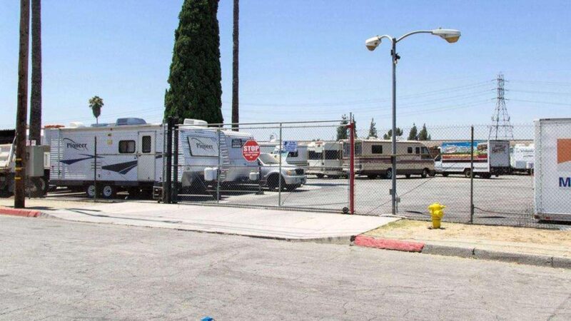 Street side view of gated entrance to outdoor parking with RVs, trailers, and trucks
