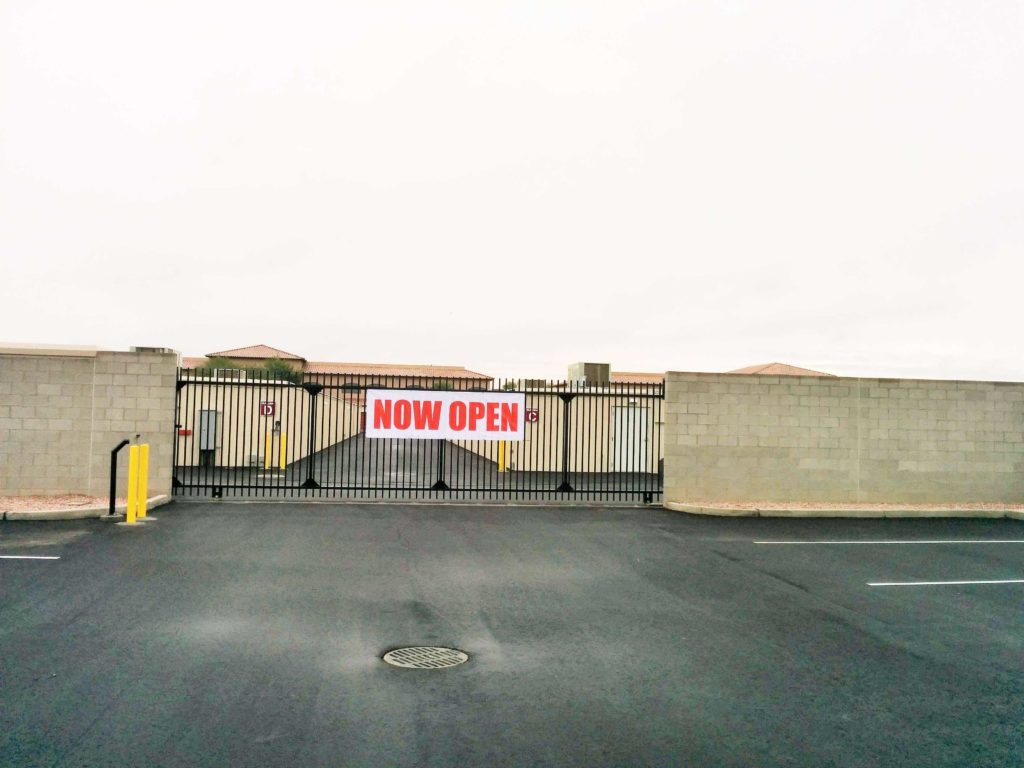 Gated entrance to outdoor storage unit with a sign on the gate saying now open