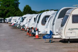 A row of RVs are parked on a paved lot in a storage facility