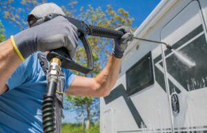 A man powerwashes the side of their RV on a bright summer day. 
