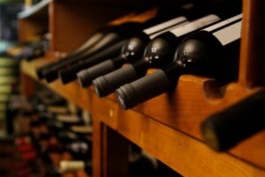 Several dark bottles of wine lay on their side in a wooden rack in storage
