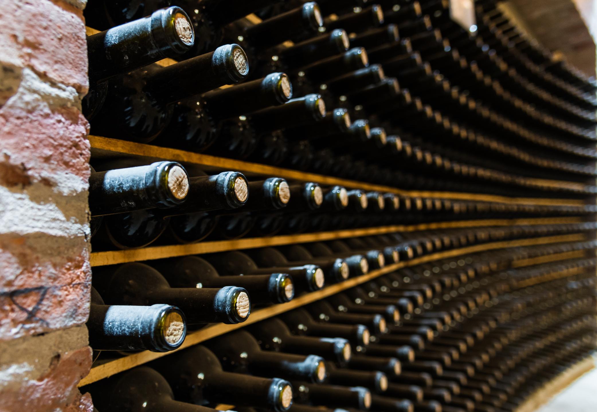 Rows of wine are kept in storage next to a brick wall
