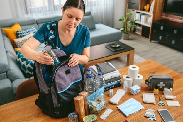 A woman packs up her emergency Go Bag, putting supplies like water bottles and first aid kits into her backpack