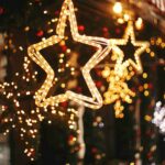 A golden star decoration glows in the evening with several other lights in bokeh.