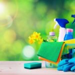A basket of cleaning supplies sits on a wooden bench with the sun shining in the background