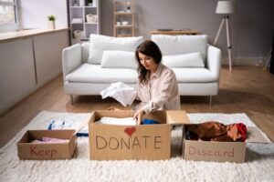 A woman sits on her living room floor next to three boxes, labeled "Keep," "Donate," and "Discard"