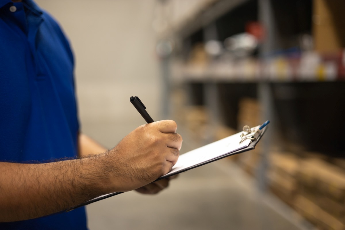 Worker reviews checklist of business inventory with pen and clipboard