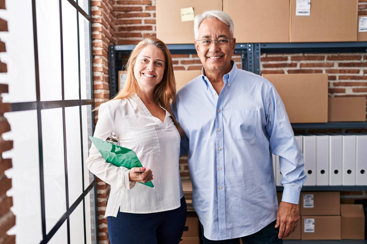 Pair of business owners hugging in front of shelves with cardboard boxes and storage items.