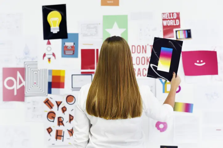 A young woman arranging colorful images and notes on a creative vision board in a bright workspace.
