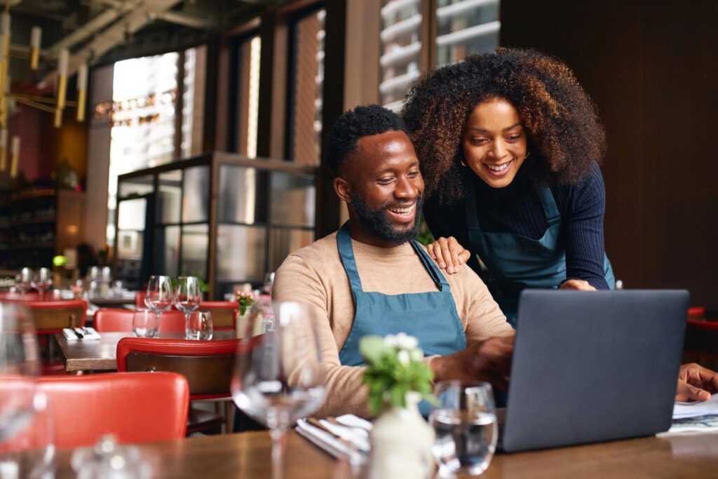 Small business partners using a laptop at a table in their restaurant.